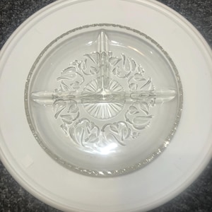 Puede incluir: Un plato de servir dividido de vidrio transparente con un patrón floral decorativo. El plato está sobre un plato blanco.