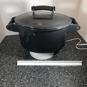 Op de afbeelding: Een donkergrijze gietijzeren braadpan met een bijpassende deksel en zwarte handgrepen. De pot staat op een wit oppervlak. Een liniaal is voor de pot geplaatst. De pot heeft een diameter van ongeveer 30 cm.