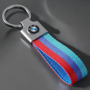 Könnte beinhalten: Ein silberner Schlüsselanhänger mit einem blau-weißen BMW-Logo und einem rot-blau-türkisen gestreiften Band.
