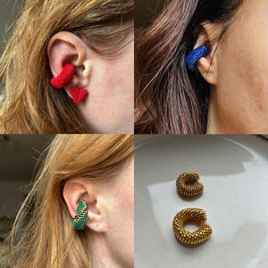 May include: An assortment of beaded ear cuffs and earrings. The image displays red heart earrings, a blue ear cuff, a green and gold ear cuff, and two gold ear cuffs. The jewellery is handmade, likely from small beads, and in various colours.