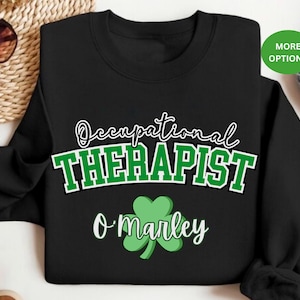 May include: Black sweatshirt with white text that reads "Occupational Therapist" and a green shamrock with the text "O'Marley" below.