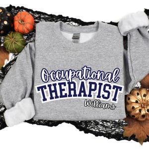 May include: Grey sweatshirt with the text "Occupational Therapist Williams" in navy blue lettering.