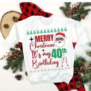 Op de afbeelding: Witte kersttrui met een rood en groen ontwerp. Er staat "Merry Christmas It's my 40th Birthday" met een cartoon kerstman met een zonnebril.