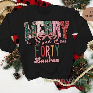 Op de afbeelding: Zwart sweatshirt met de woorden "MERRY and FORTY" in een feestelijk, kleurrijk ontwerp. Het ontwerp bevat een strik en het jaar "1985", met de naam "Lauren" eronder. De sweatshirt heeft lange mouwen en een ronde hals.