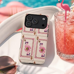 May include: A phone case with a flamingo pattern, a pink drink with a flamingo straw, and sunglasses are on a white surface near a pool. The phone case has a repeating design of pink flamingos in decorative frames.