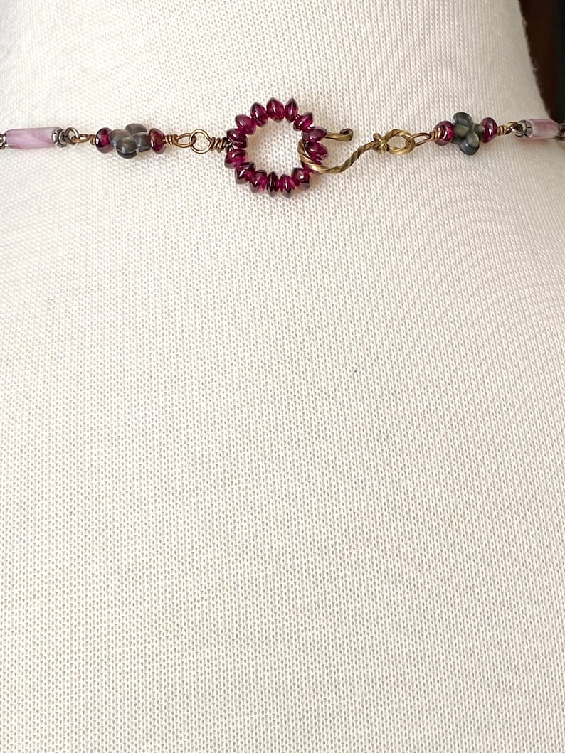 May include: A close-up of a necklace clasp with a circle of small red beads and a hook closure. The necklace is made with wire and has other beads in shades of gray and pink.