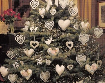 Puede incluir: Un árbol de Navidad decorado con adornos en forma de corazón. El árbol está adornado con corazones de encaje y tela blancos, estrellas y adornos de ángeles. Un gran lazo blanco se encuentra en la parte superior, rodeado de vegetación y pequeñas flores blancas.