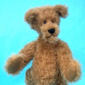 May include: A handmade, brown teddy bear with a shaggy fur texture. The bear has a black nose, small black eyes, and tan paw pads. It stands upright against a light blue background, showcasing its unique, handcrafted design.