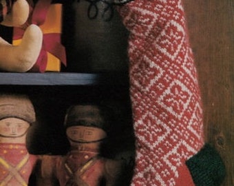 Op de afbeelding: Een rood-witte gebreide kerstsok met een groene boord. De sok hangt aan een houten plank met een knuffeldier en een cadeaudoos.