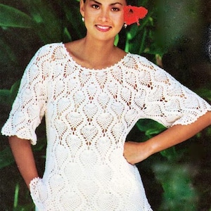 May include: White crochet top with a delicate, lacy pattern. The top has a round neckline and short sleeves.