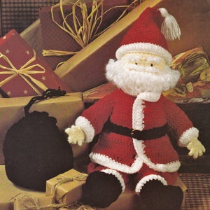 Könnte beinhalten: Gehäkelte Weihnachtsmann-Puppe in rotem Anzug mit weißer Bordüre, schwarzem Gürtel und schwarzen Stiefeln. Die Puppe hat einen weißen Bart und eine rote Mütze mit weißer Quaste. Geschenke, verpackt in braunem und rotem Papier mit goldenen Sternen, umgeben die Puppe.