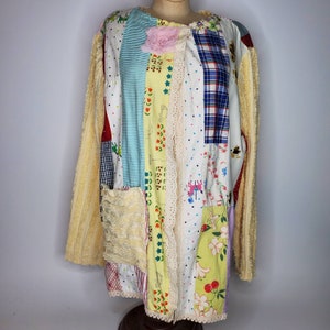May include: A long, cream-colored patchwork jacket with a variety of colorful fabrics, including floral, plaid, and polka dot patterns. The jacket has a lace trim and a flower embellishment.