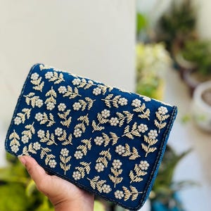 May include: A dark blue clutch purse with a floral design embroidered with white pearls and gold beads.