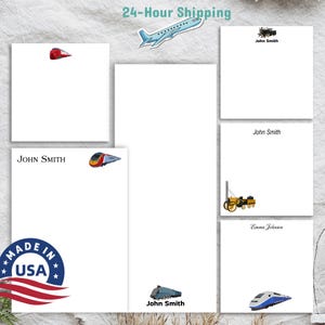 May include: White notepads with train and construction vehicle illustrations. The notepads have the text "John Smith" and "Emma Johnson". A "Made in USA" sticker is visible. A sticker of an airplane is also visible.