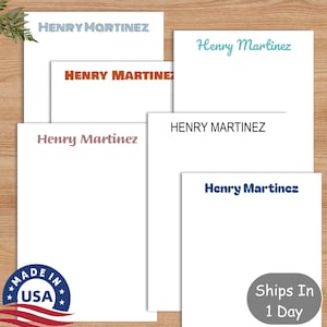 May include: Five white notepads with the name "Henry Martinez" printed in different colors and fonts. The notepads are stacked on top of each other. The bottom notepad has a "Made in USA" label.
