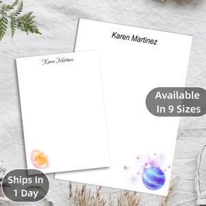 May include: Two white notepads with the name "Karen Martinez" printed in black. One notepad has a watercolor design of a planet in the corner. The other notepad has a watercolor design of a planet and stars. Text on the image says "Available In 9 Sizes" and "Ships In 1 Day".