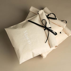 May include: Stack of three white canvas bags with black ribbon ties. The top bag has the word "Mason" embroidered in white on the front.