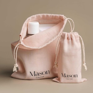 May include: Two pink drawstring bags, one open and filled with a white bottle and other items. The smaller bag is closed. Both bags have the text "Mason Cute Craft" printed in black.