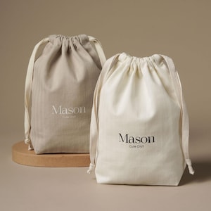 May include: Two fabric drawstring pouches, one in beige and one in off-white. Each bag features the text Mason Cute Craft printed on the front. The beige bag has white text, while the off-white bag has black text. Both bags have matching fabric drawstrings.