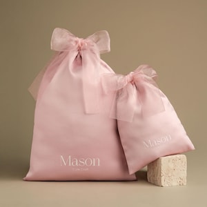 Puede incluir: Dos bolsas de regalo de sat&eacute;n rosa con lazos de cinta transparente. La bolsa m&aacute;s grande tiene la palabra "Mason" impresa, con "Cute Craft" debajo. La bolsa m&aacute;s peque&ntilde;a tambi&eacute;n tiene la palabra "Mason" impresa. Las bolsas est&aacute;n sobre un fondo neutro.