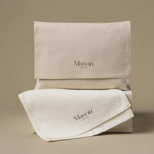 Puede incluir: Dos bolsas de tela beige, una plegada y otra plana, apiladas sobre una caja blanca. La palabra "Mason" y "Cute Craft" están impresas en marrón en ambas bolsas. La tela tiene una textura sutil.