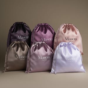 May include: A collection of six satin drawstring pouches in various shades including dark purple, mauve, light pink, taupe, dusty rose, and lavender. Each pouch features a white printed logo that reads Mason Cute Craft on the front.