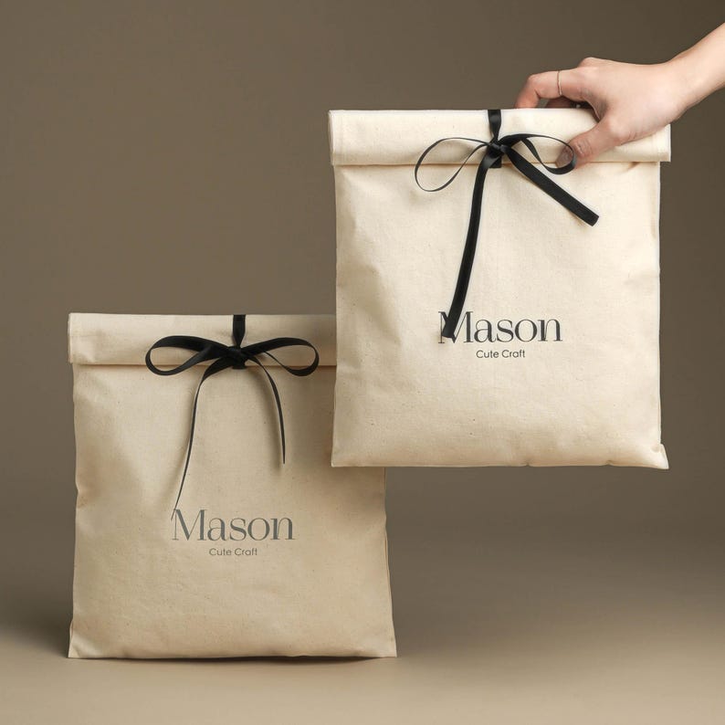 May include: Two beige gift bags with black ribbon bows and the text "Mason Cute Craft" printed on the front.