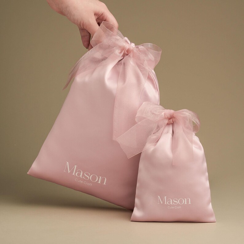 Puede incluir: Dos bolsas rosas de sat&eacute;n con lazos de cinta transparente. La bolsa m&aacute;s grande tiene la palabra "Mason" y "Cute Craft" impresa en blanco. La bolsa m&aacute;s peque&ntilde;a tambi&eacute;n tiene la palabra "Mason" y "Cute Craft" impresa en blanco.
