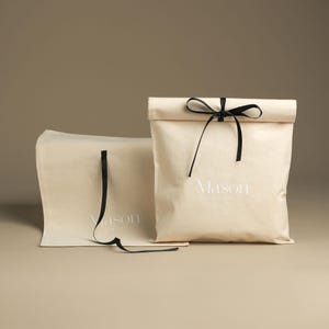 May include: Two beige fabric gift bags with black ribbon ties. The bags have the text "Mason" printed on them in white.