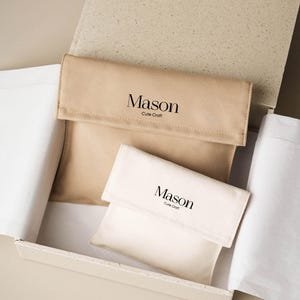 May include: Two rectangular fabric pouches with fold-over flaps, one tan and one cream, both featuring the black printed text Mason Cute Craft. The pouches are nestled inside a light beige cardboard box lined with white tissue paper.