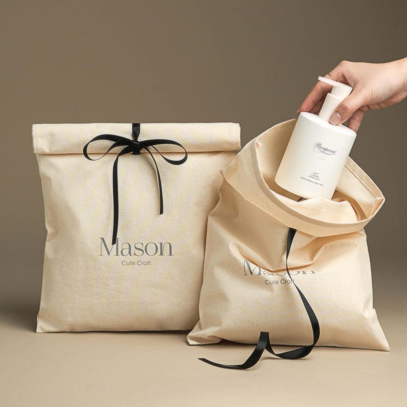 May include: Two beige fabric gift bags with black ribbon ties. The bags have the text "Mason Cute Craft" printed on them. One bag has a white bottle of hand soap inside.