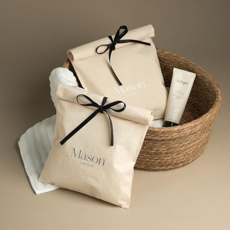 May include: Two white canvas bags with black ribbon ties and the text "Mason Cute Craft" printed on them. The bags are in a woven basket with a white tube of lotion.