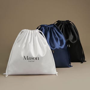 May include: Three satin drawstring bags in white, navy blue, and black. The white bag has the text "Mason Cute Craft" printed in black. The navy and black bags have the letter "n" printed in gold.