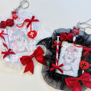 Puede incluir: Dos accesorios decorativos con ilustraciones de estilo anime. Uno es blanco con un lazo rojo, rosas y una jeringa. El otro es negro con un lazo rojo, rosas y una jeringa. Ambos tienen un dije de bolsa de sangre y una imagen de dibujos animados.