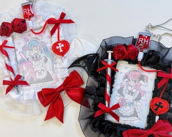 May include: Two decorative accessories with anime-style illustrations. One is white with a red bow, roses, and a syringe. The other is black with a red bow, roses, and a syringe. Both have a blood bag charm and a cartoon image.