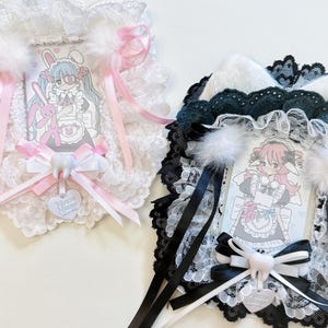 May include: Two decorative frames with cartoon illustrations. One is white with pink accents, the other black with white accents. Both have lace trim, bows, and a tooth-shaped charm. The illustrations depict anime-style characters.