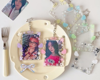 May include: Clear acrylic keychains with star and cloud accents, holding photos of women. The keychains have silver-colored chains and are decorated with pastel-colored embellishments. One photo is of a woman with red hair and glasses.