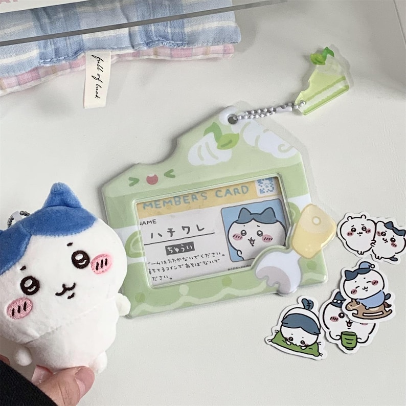 May include: A collection of cute, cartoon-style accessories. Includes a light green member's card holder with a cartoon character, a plush toy with a blue and white design, and several stickers. The card holder has Japanese text.