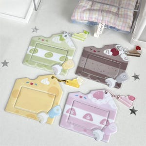 May include: Four colorful cake-shaped ID badge holders. The holders are in shades of green, brown, yellow, and pink, each with a different cake slice design. Each holder has a small charm and a clear window for an ID card.