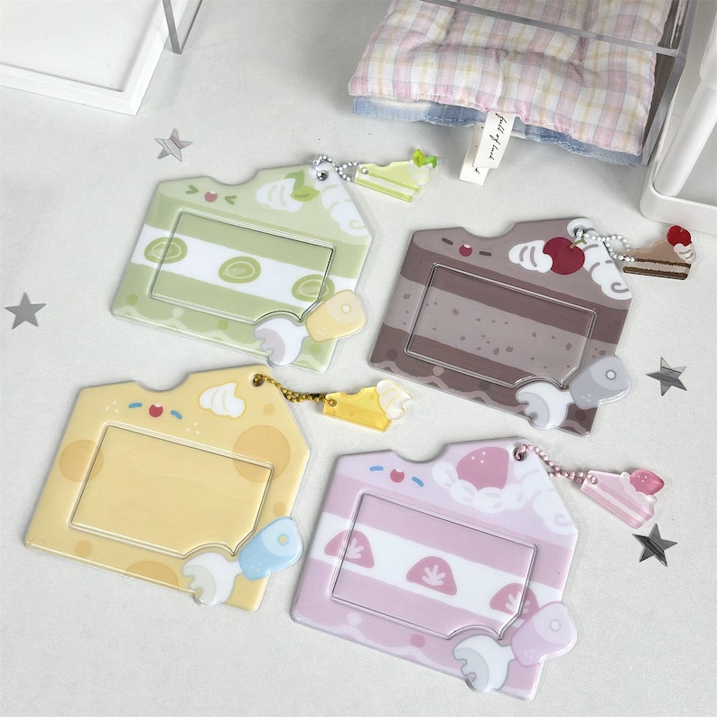 May include: Four colorful cake-shaped ID badge holders. The holders are in shades of green, brown, yellow, and pink, each with a different cake slice design. Each holder has a small charm and a clear window for an ID card.