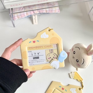 May include: A yellow, house-shaped plastic card holder featuring a cartoon cheese design with a small blue fork accent. Inside is a member's card with Japanese text and a rabbit illustration. A small plush rabbit toy is attached to the side.