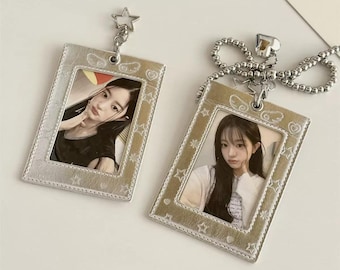 May include: Two rectangular photo card holders with a metallic silver finish and embossed star and heart patterns. Each holder features a clear window displaying a portrait of a person. One holder has a star charm, the other a beaded chain.