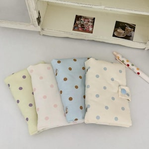 May include: Four rectangular fabric pouches with snap closures, each featuring a polka dot pattern. The colors include a pale yellow with purple dots, a white with pink dots, a light blue with brown dots, and a cream with light blue dots.