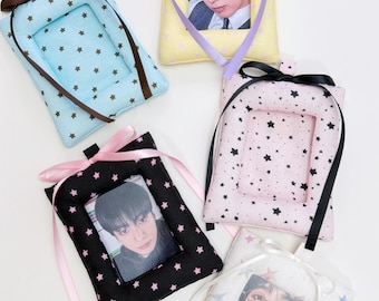 May include: Five rectangular fabric photo holders featuring star patterns in light blue, yellow, pink, black, and white. Each holder includes a ribbon bow at the top and a clear window displaying a portrait of a person. The fabric frames are padded.