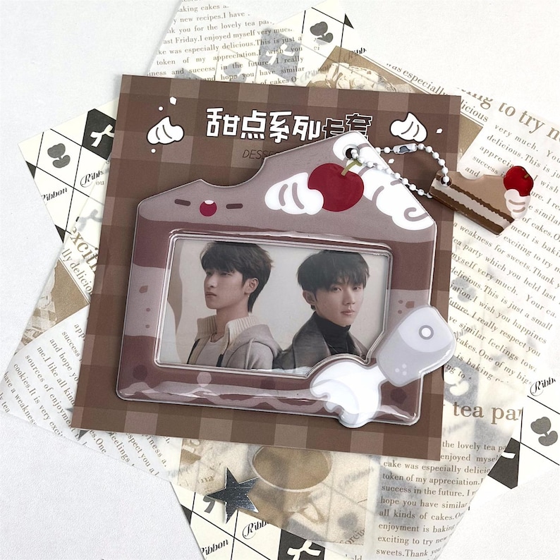May include: A brown photo frame shaped like a house with a cherry and cake charm. The frame holds two photos of young men. The text "甜点系列安" is visible on the frame. The background includes printed paper.