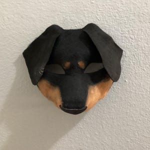 May include: A handmade dog mask with a black head and ears, and a tan muzzle. The mask has eye openings and is likely made of felt or a similar fabric. It is designed to be worn.