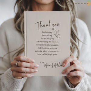 May include: A beige hardcover book with dark brown text that reads: Thank you, For listening, For teaching, For encouraging, For celebrating the victories, For supporting the struggles, And thank you for seeing potential, Love: Aria Miller.