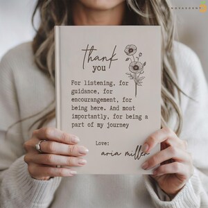 May include: A light beige book with dark brown text that reads: Thank you. For listening, for guidance, for encouragement, for being here. And most importantly, for being a part of my journey. Love: aria miller. A line drawing of flowers is included.