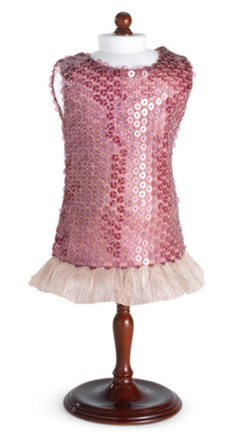 Pu&ograve; includere: Un abito rosa con paillettes e un orlo a balze di tulle, esposto su un manichino di legno.