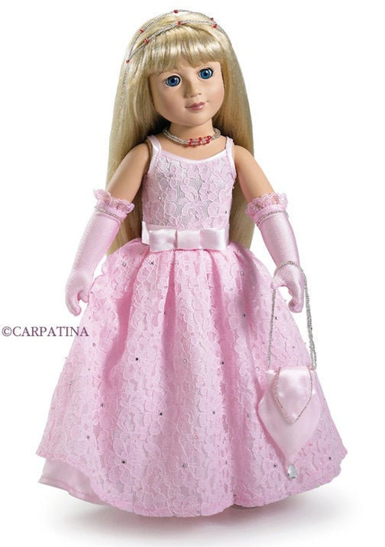 May include: A doll with long blonde hair, blue eyes, and a pink lace dress. The doll wears a tiara, necklace, and gloves, and carries a small purse. The dress has a white bow at the waist and is adorned with sequins.